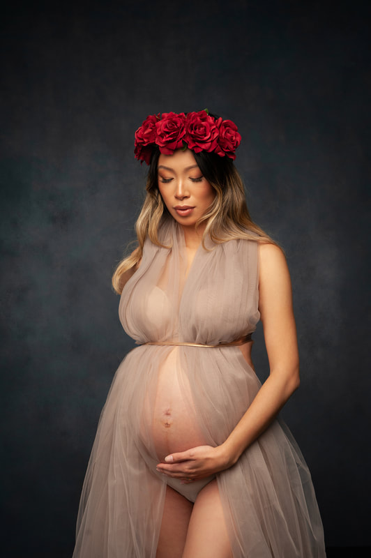 maternity photoshoot, expectant mother with red flower crown wearing long lashes and chiffon dress in studio textured background