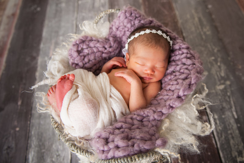 newborn photography baby girl wrapped in basket with fur on wooden floors